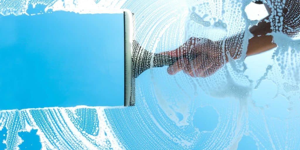 A hand uses a squeegee to clean a soapy window, revealing a clear blue background—perfect for showcasing professional pressure washing in Montgomery County, MD.